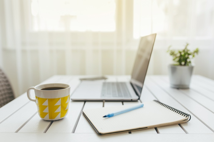 laptop on desk next to pad of paper and pen and coffee mug