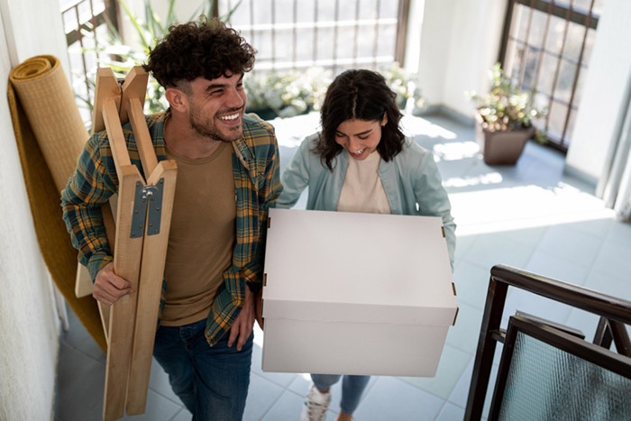 Couple moving into a house carrying boxes and furniture