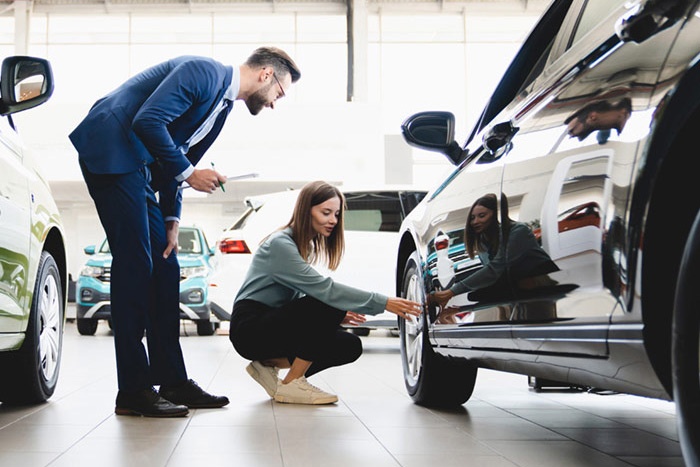 Man and woman in car dealership examining the wheel on a car