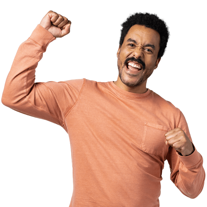 Young man cheering with a fist pump and an excited face. He sports a moustache, a short afro hairstyle, and a salmon-colored long sleeve t-shirt.